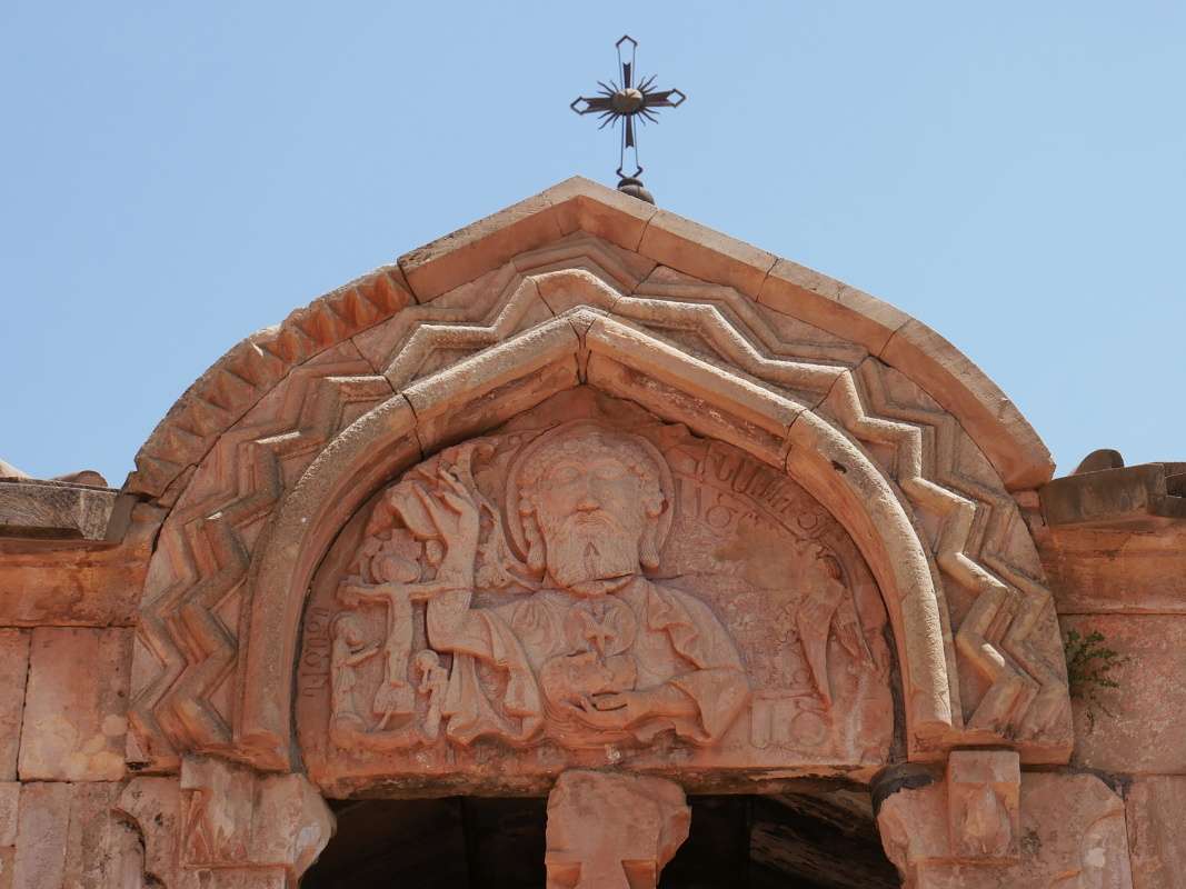 Noravank - kostol Surb Karapet, Boh Otc s veľkými mandľovými očami, pravou rukou žehná kríž a v ľavej ruke drží hlavu Jána Krstiteľa s holubicou – Duchom Svätým 